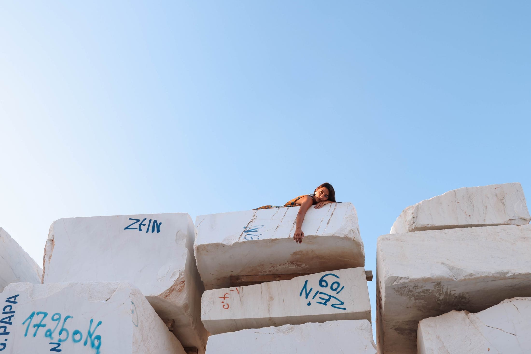 A figure draped over a marble block among the stacked blocks of the Zein Group yard