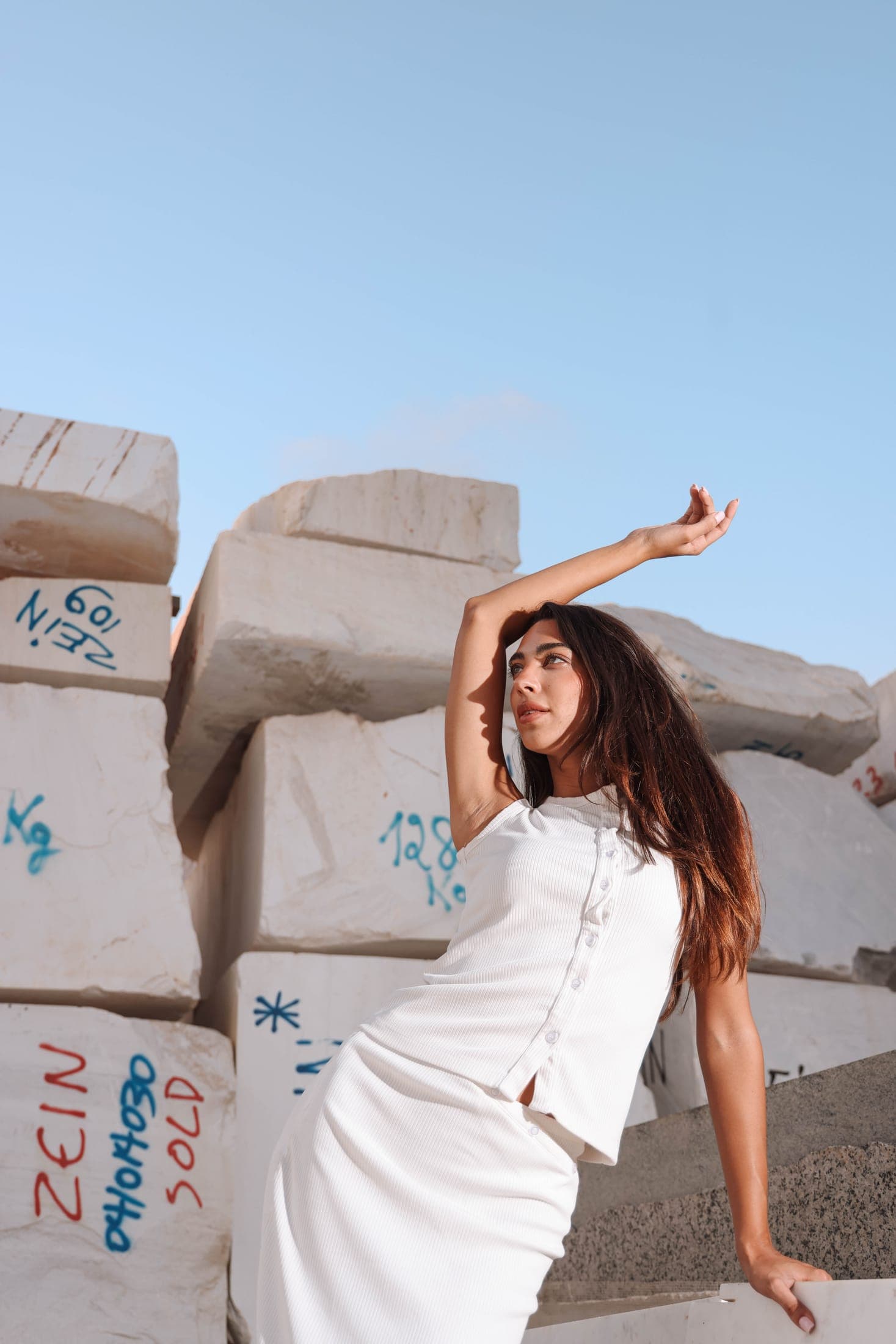 A figure in white among ZEIN-marked marble blocks, seen from a low angle