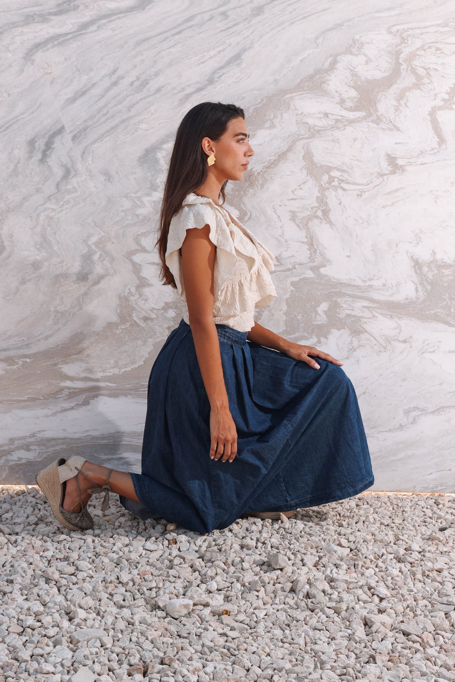 A figure in a white top and denim skirt kneeling before a grey-veined white marble slab