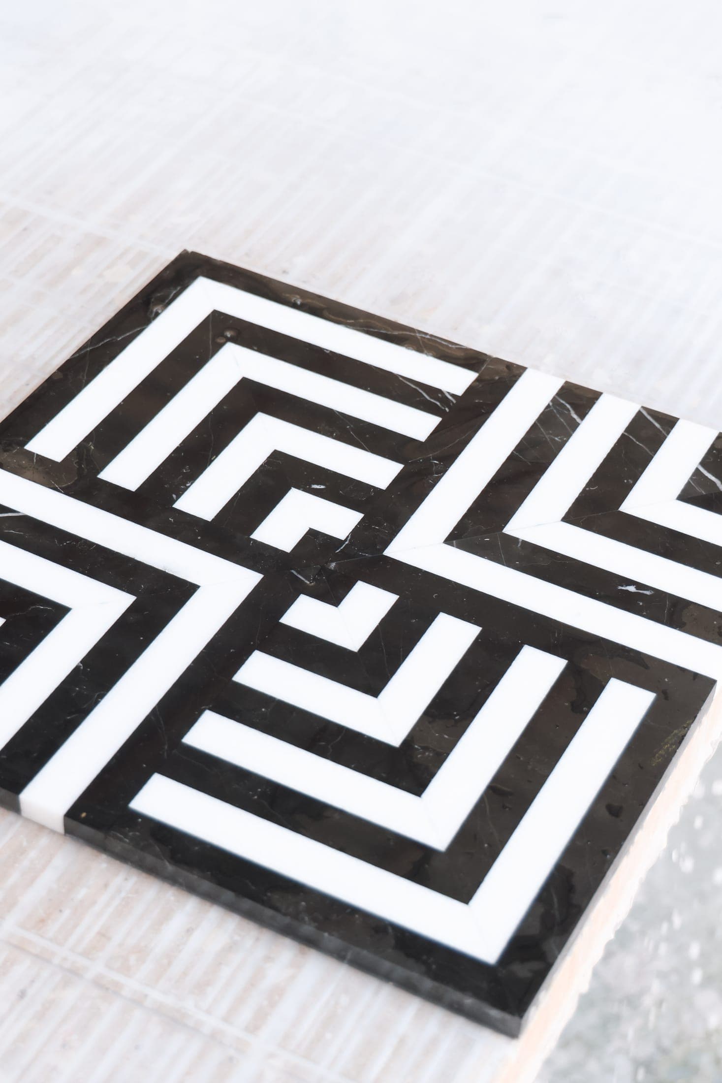 A black-and-white marble inlay tile with a geometric labyrinth pattern
