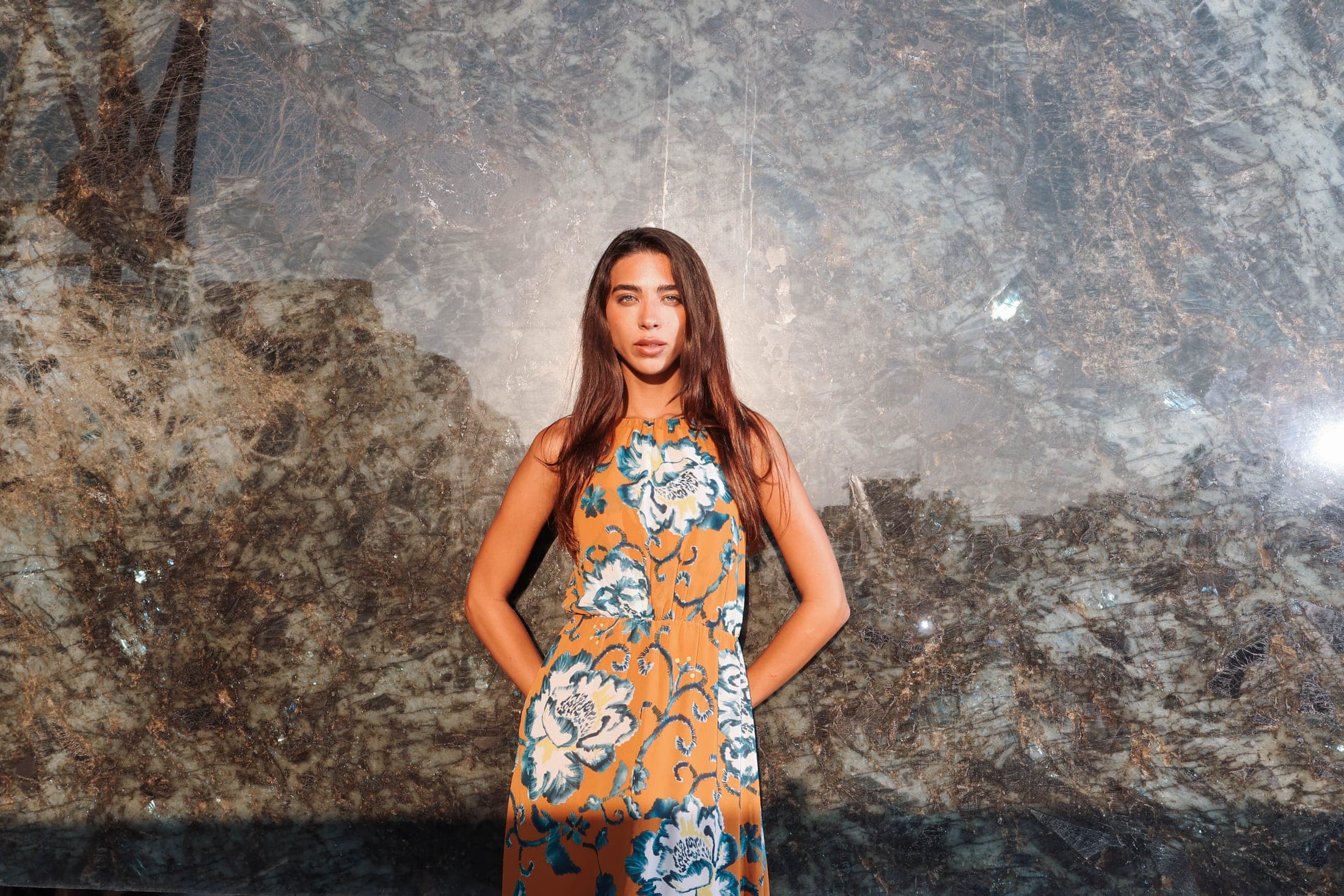 A figure in a floral dress before a vast polished dark slab at the Zein Group yard — still from the Zein Group film