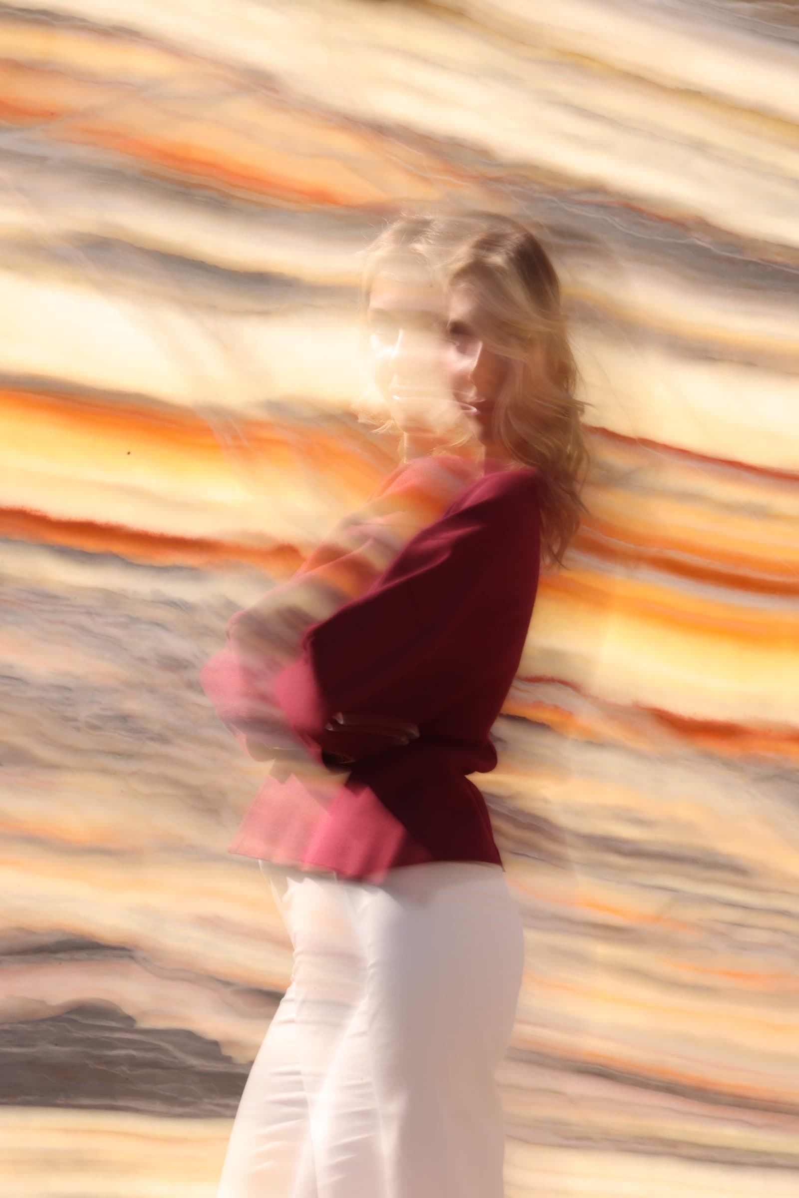 A figure in burgundy moving past streaking golden onyx — motion blur