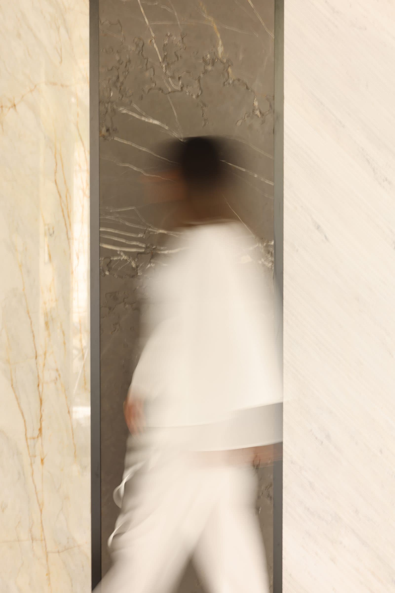 A figure in white blurred in motion past a marble wall