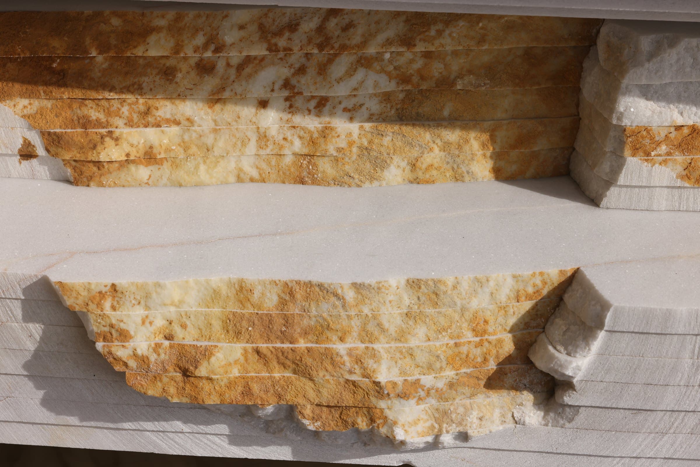 Raw split-face stone blocks with warm gold and cream veining, freshly cut from the quarry