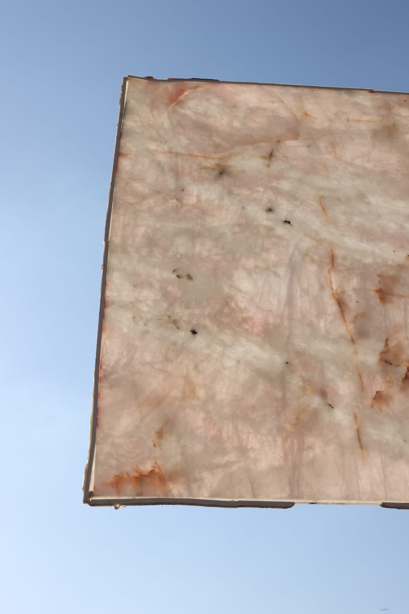 Pale crystalline quartzite slab raised at an angle against the blue sky