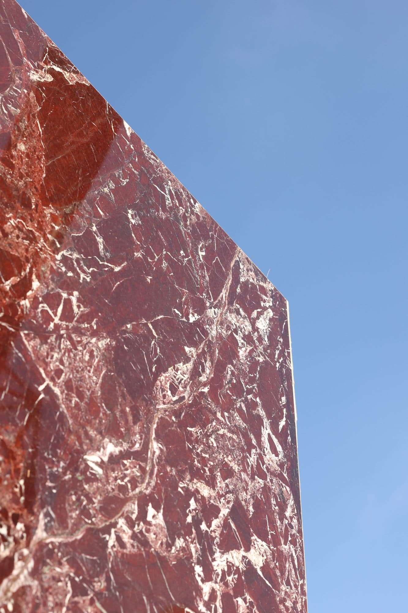 Deep-red marble slab raised at an angle against the blue sky at the Zein Group stone yard