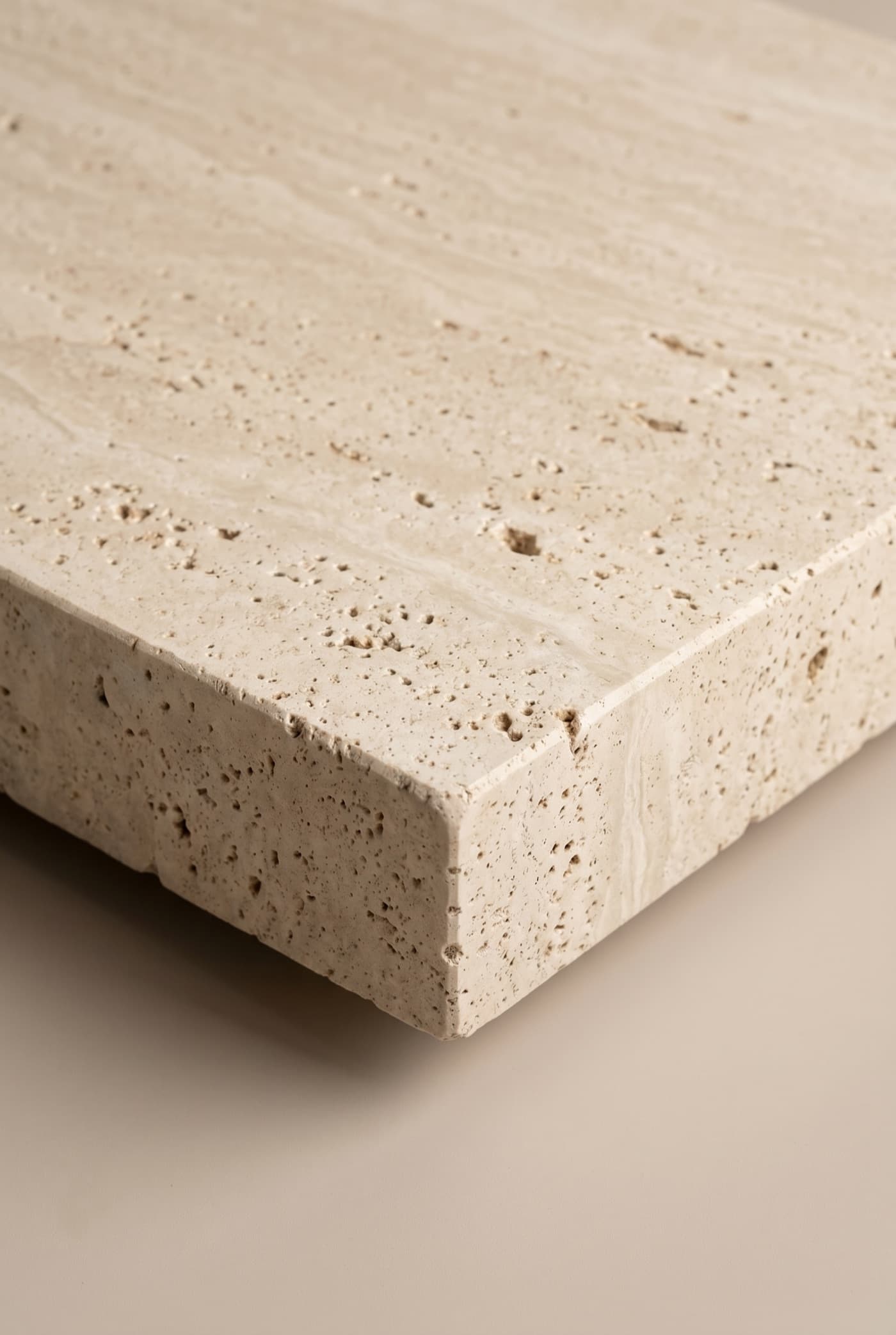 Honed travertine block with a clean cut edge profile and natural open pores, photographed in soft studio light