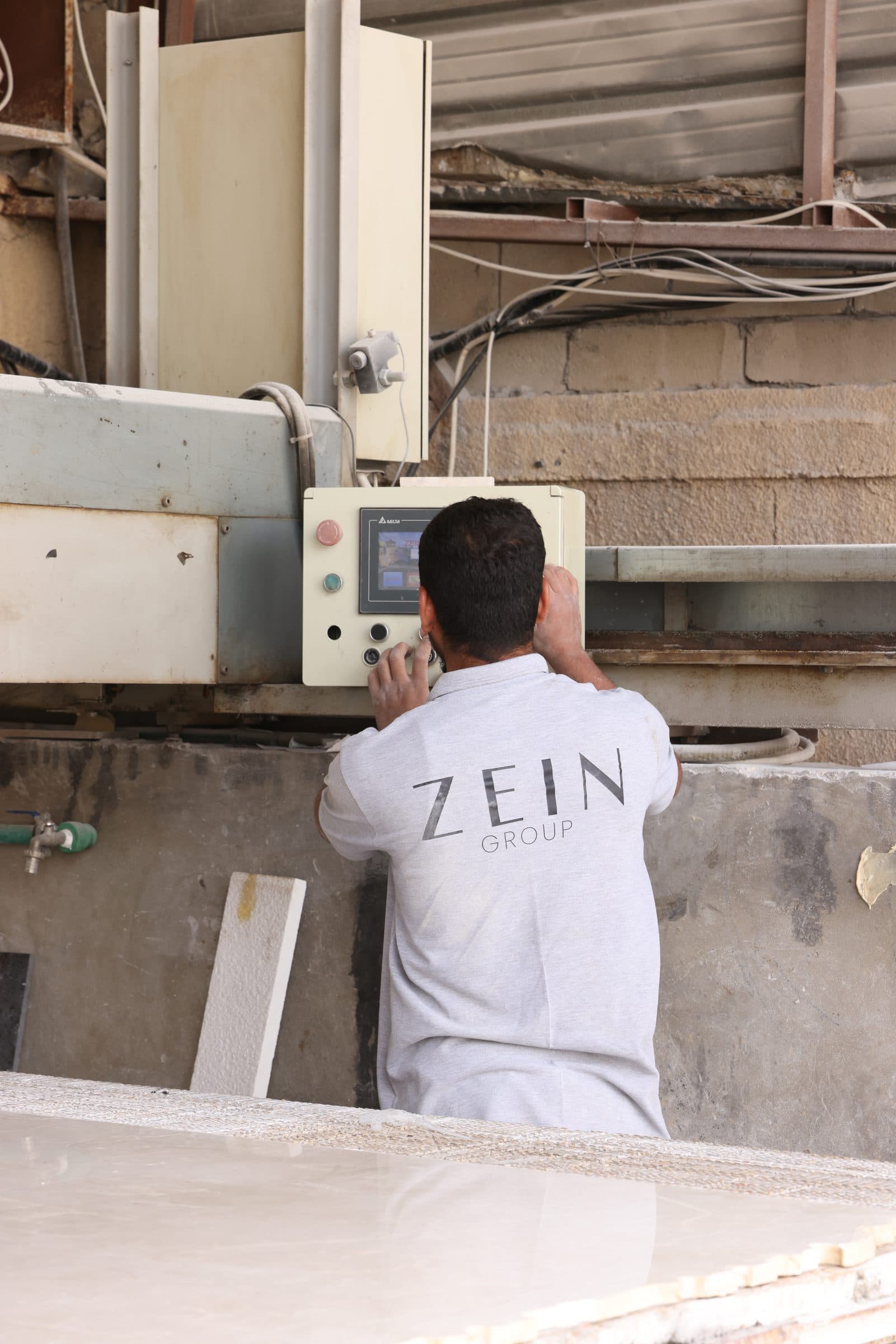 Craftsman in a Zein Group shirt working the stone saw, Beirut workshop