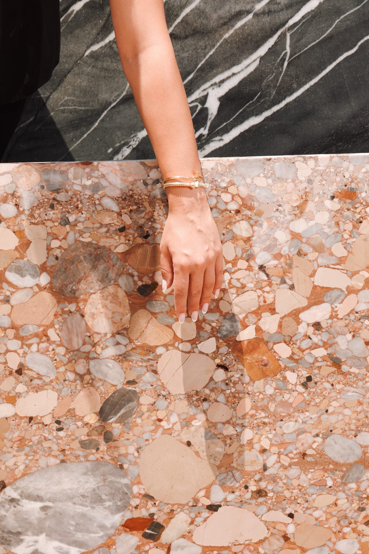 A hand on a polished breccia slab, with black marble behind it