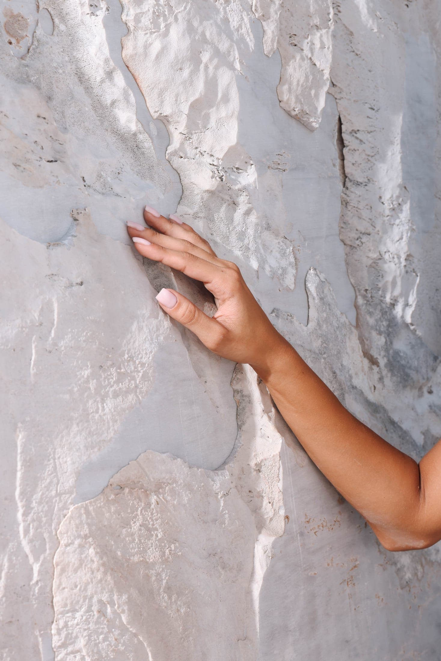 A hand resting on the rough split face of a white stone block