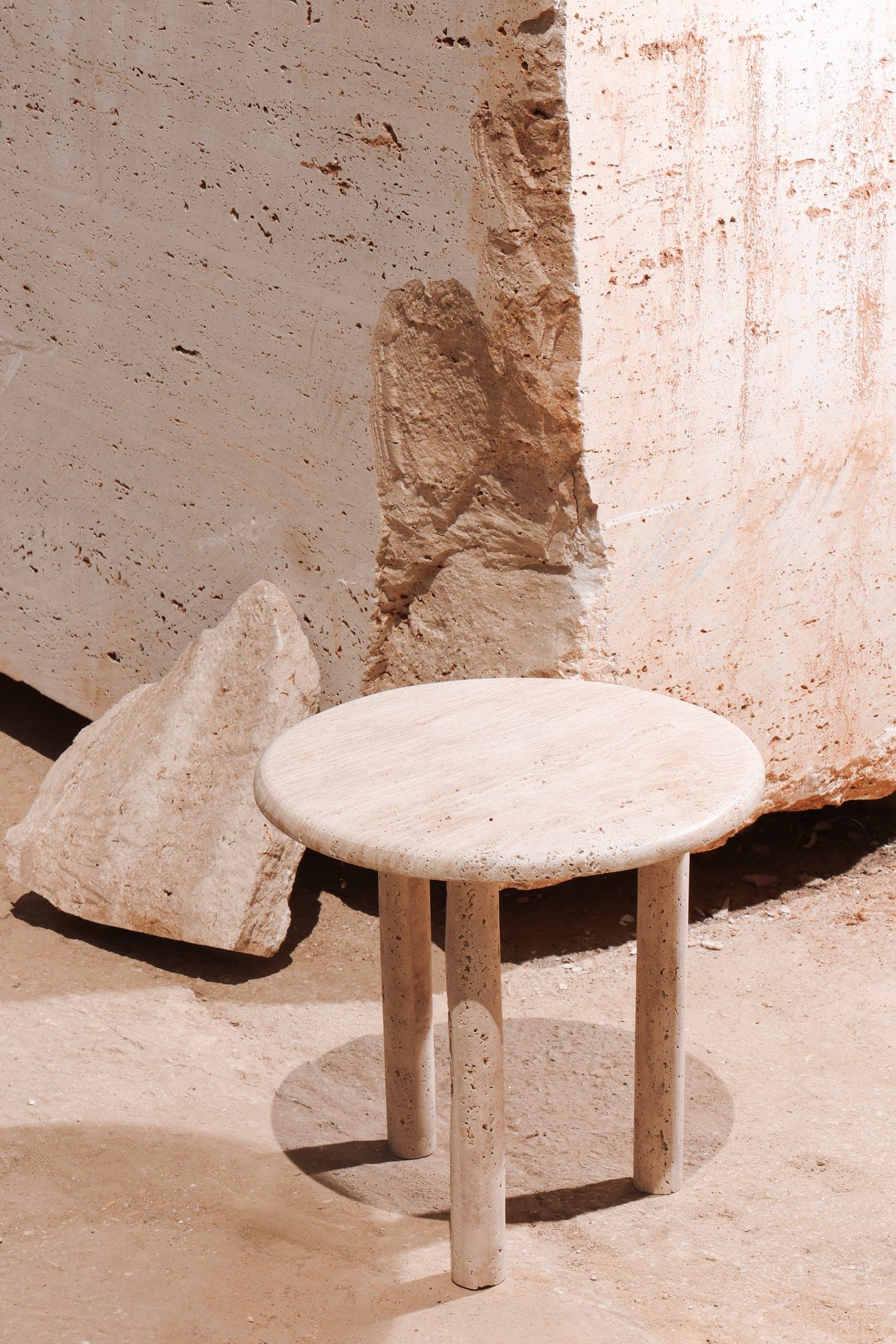 A turned travertine side table standing beside a raw stone block at the Zein Group yard