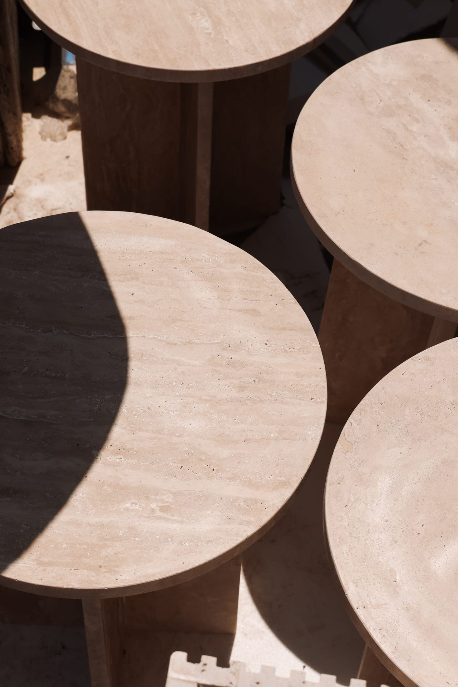 Round travertine side tables in hard sunlight at the Zein Group atelier