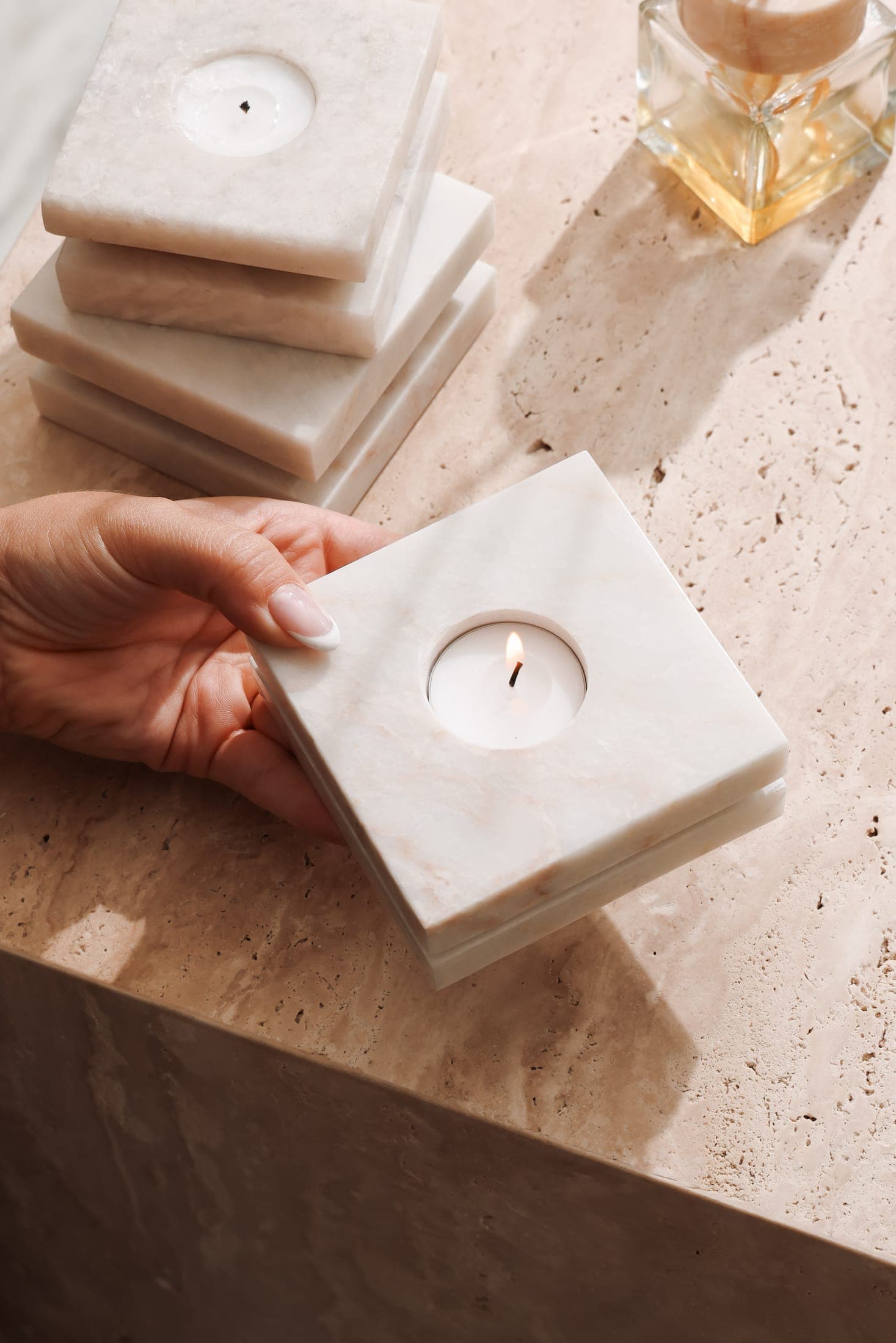 A white marble tealight holder held in hand over a travertine counter